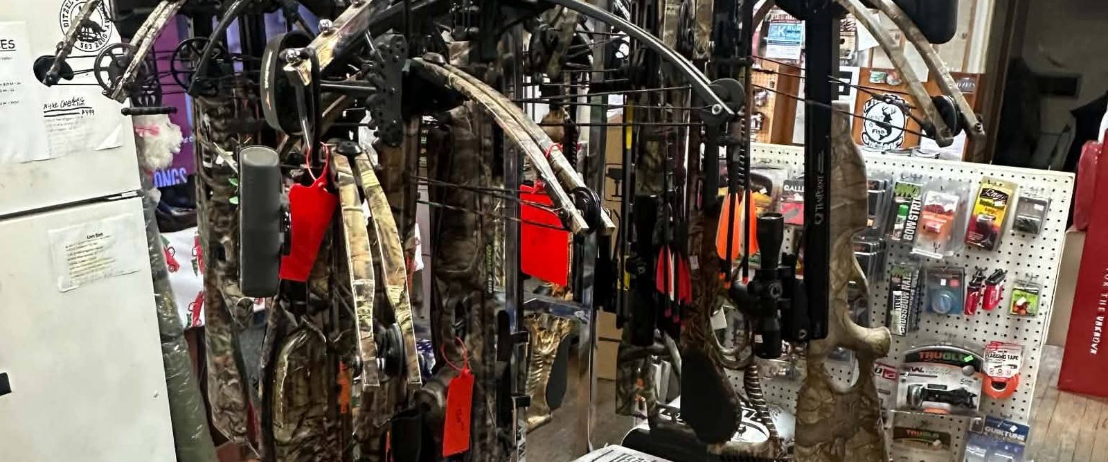 Bow rack inside Litchfield Outdoors — compound bows and crossbows above stacked archery targets, with a mounted deer on the wall.