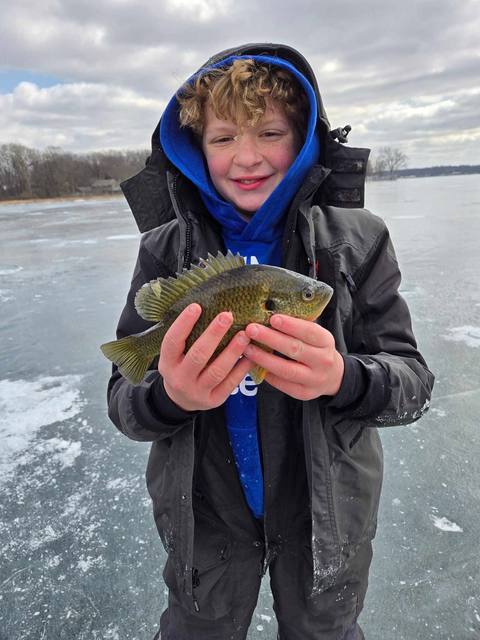Two anglers kneeling on the ice holding tagged walleye and perch in front of the local sponsor board at a Litchfield Outdoors community event.