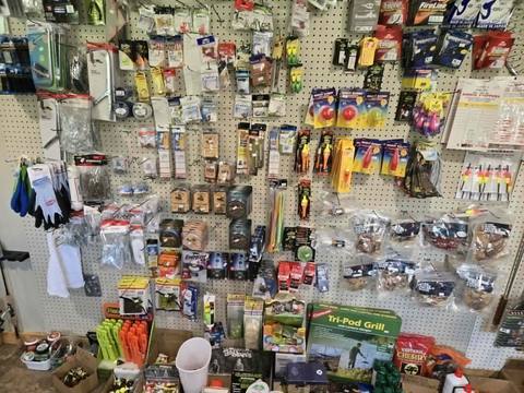 Tackle pegboard wall at Litchfield Outdoors: fishing line, bobbers, gloves and packaged lures, with grills and accessories below.