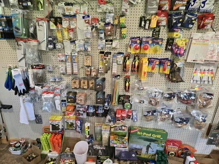 Tackle pegboard wall at Litchfield Outdoors: fishing line, bobbers, gloves and packaged lures, with grills and accessories below.