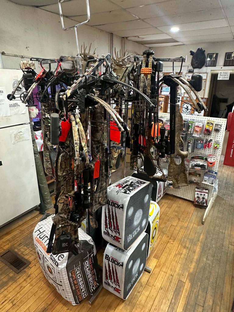 Compound bows on the rack inside Litchfield Outdoors above stacked archery targets.